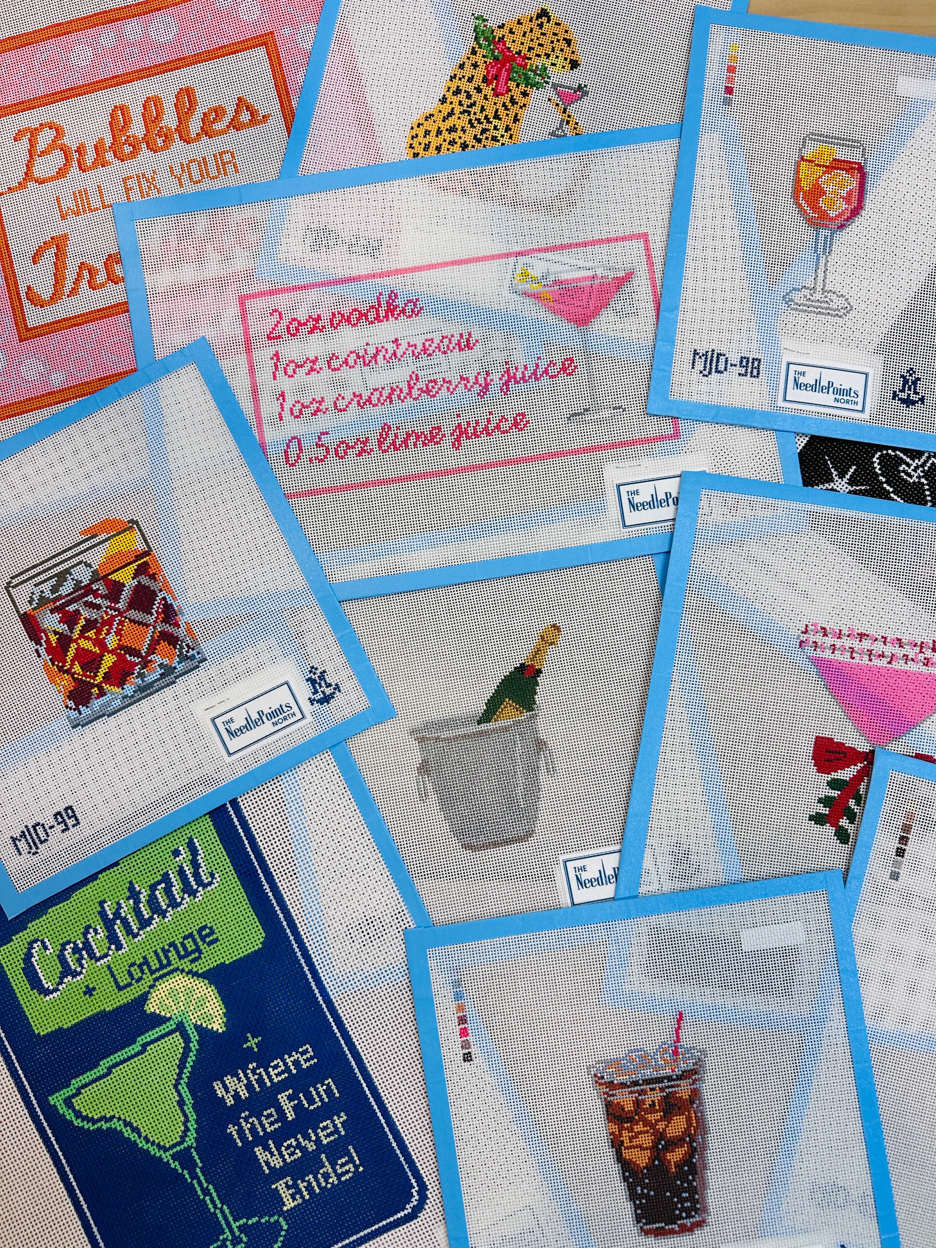 Collection of needlepoint canvases featuring cocktail-themed designs on a textured surface.