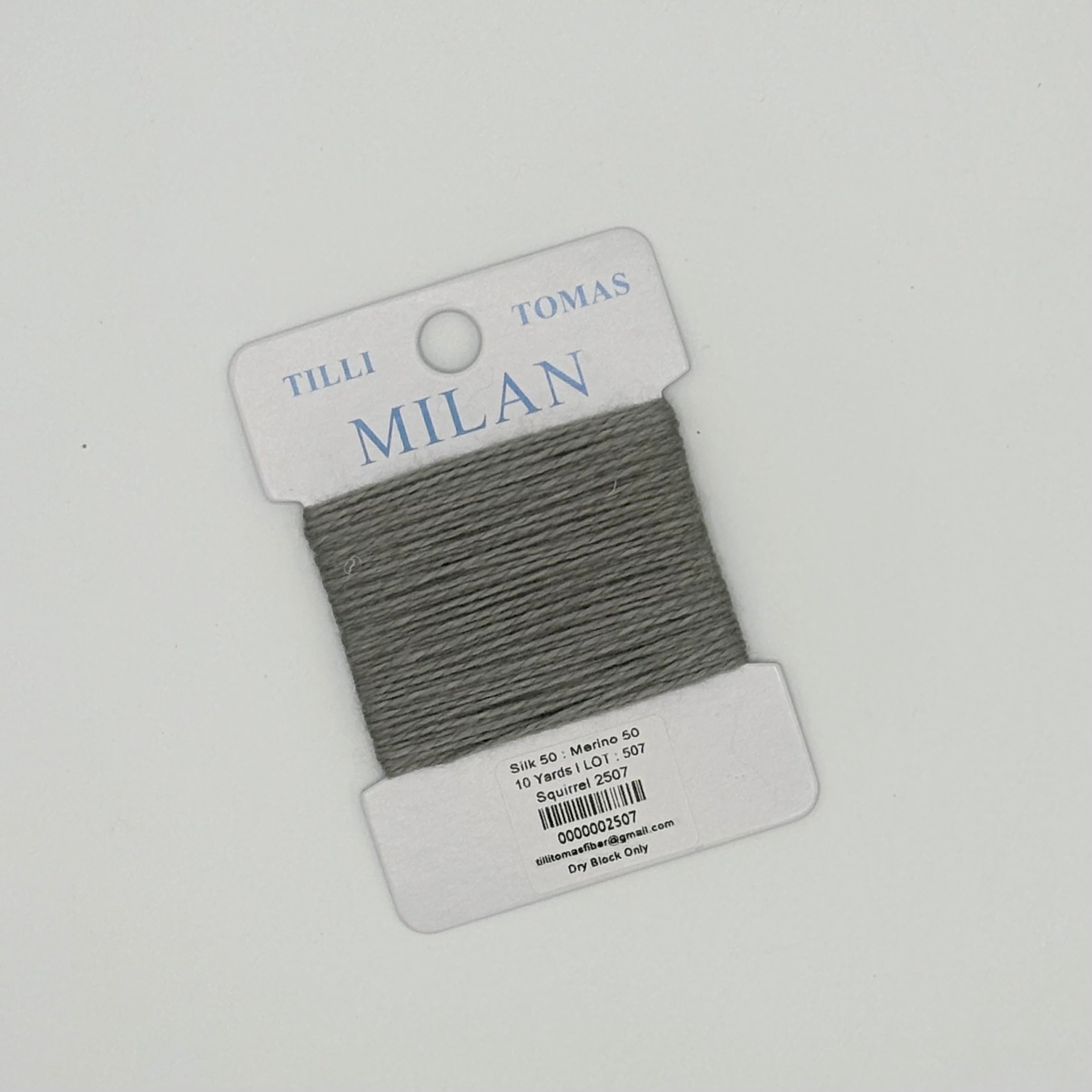 Gray thread on a Tilli Tomas Milan label against a light gray background