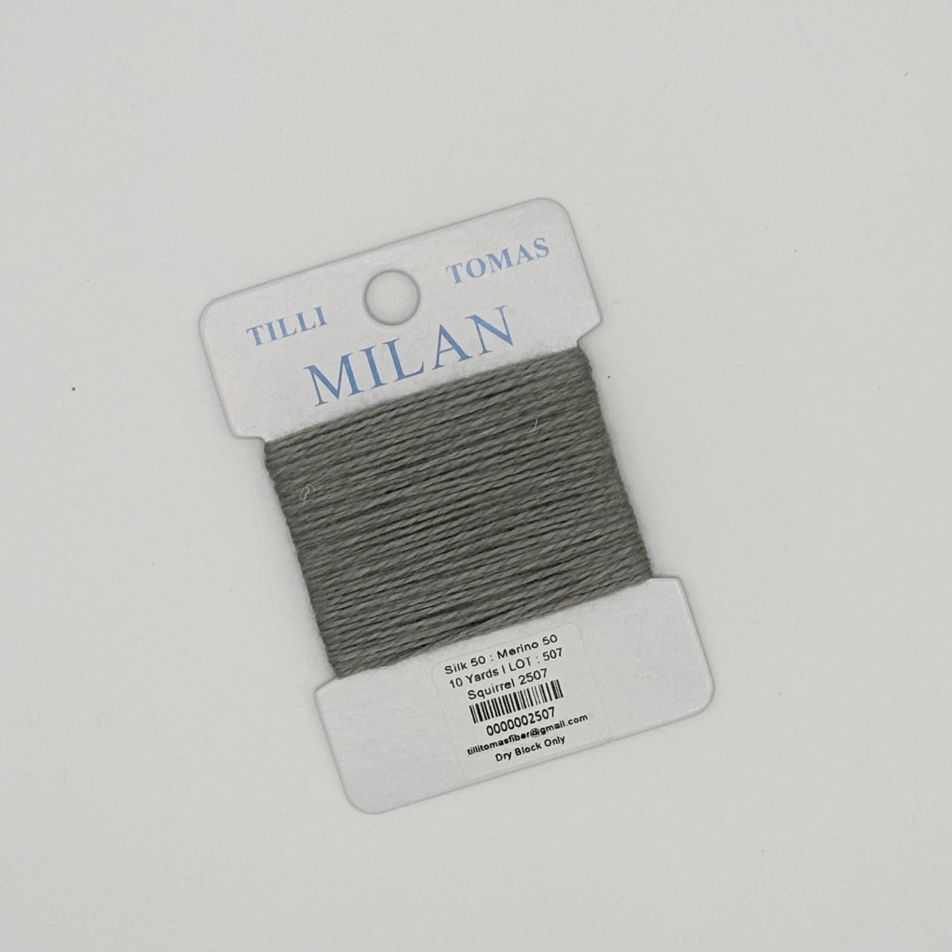 Gray thread on a Tilli Tomas Milan label against a light gray background