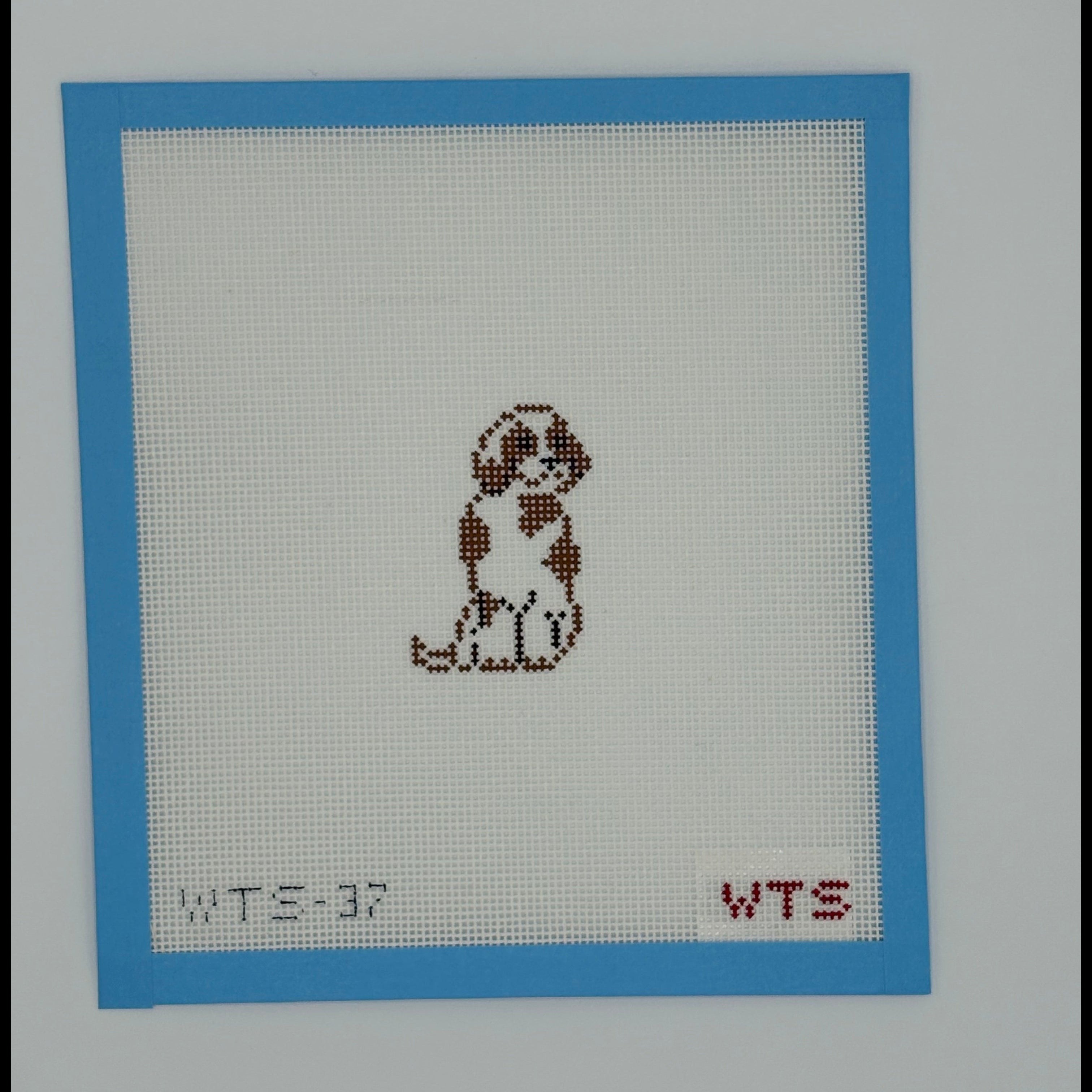 Needlepoint design of a dog on fabric with a blue border and red text.