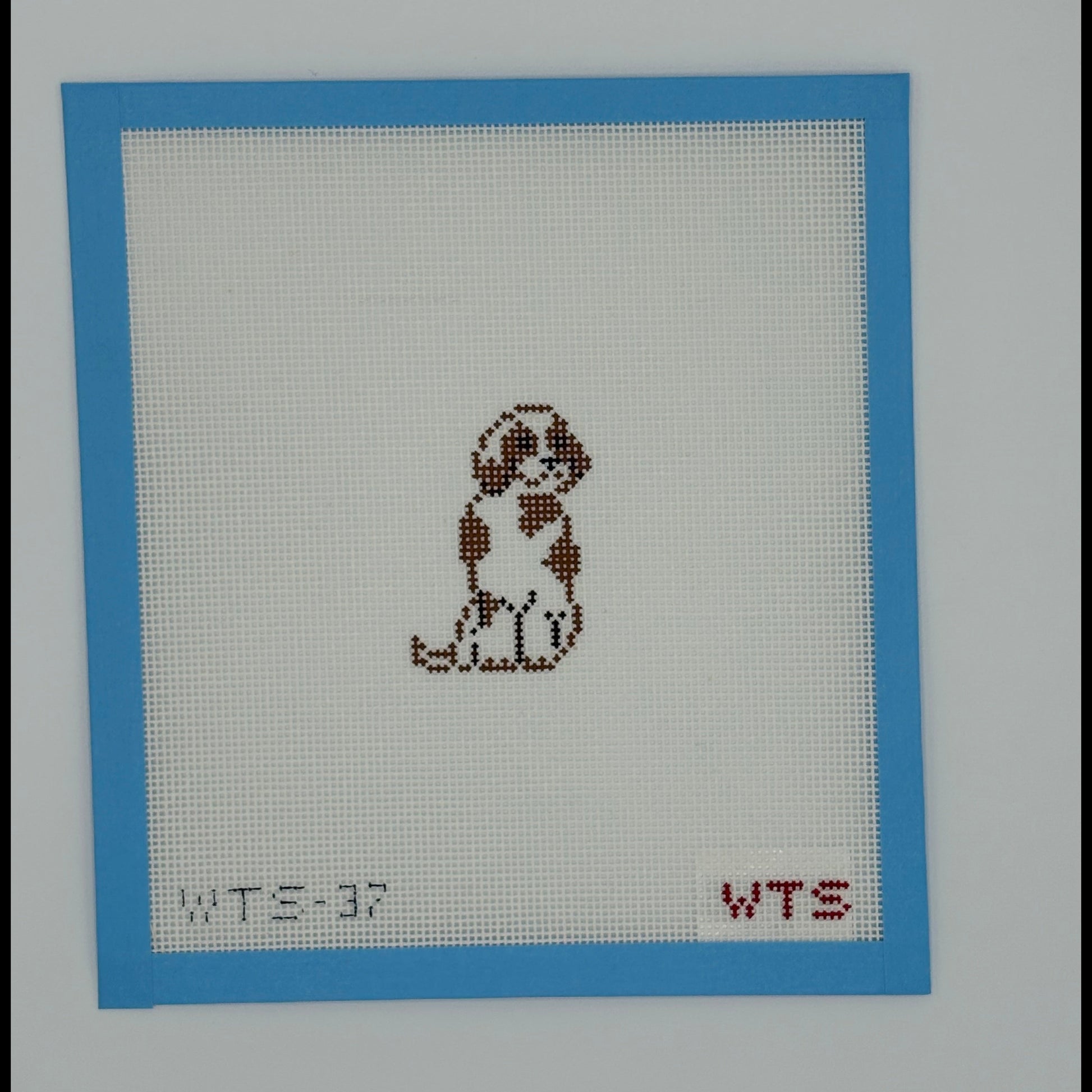 Needlepoint design of a dog on fabric with a blue border and red text.