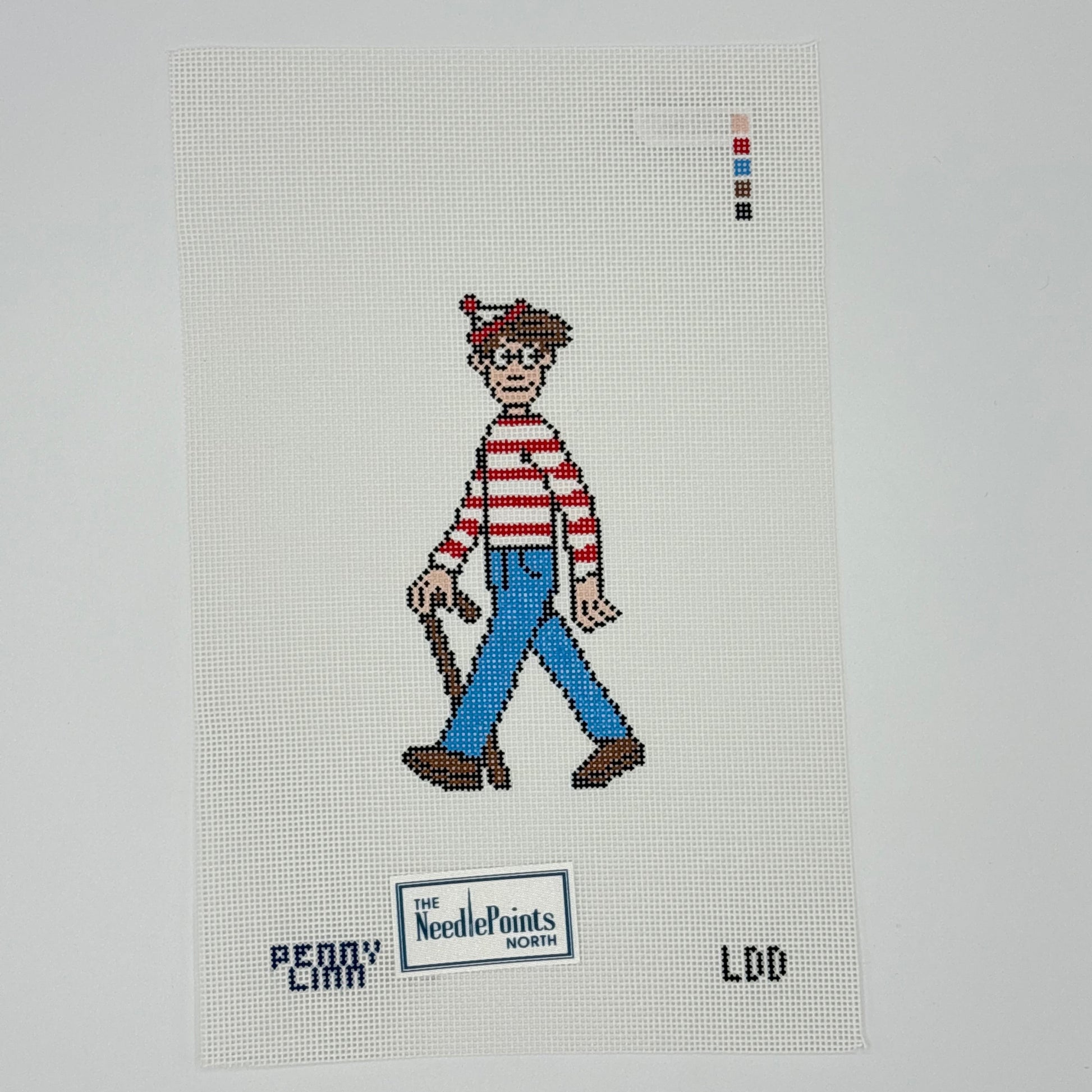 A needlepoint canvas featuring a pixelated depiction of the character 'W' from 'The Needlepoints of Hollywood' wearing his signature red and white striped shirt, blue pants, and brown shoes, with 'PENNY CARR' and 'LDD' printed below.