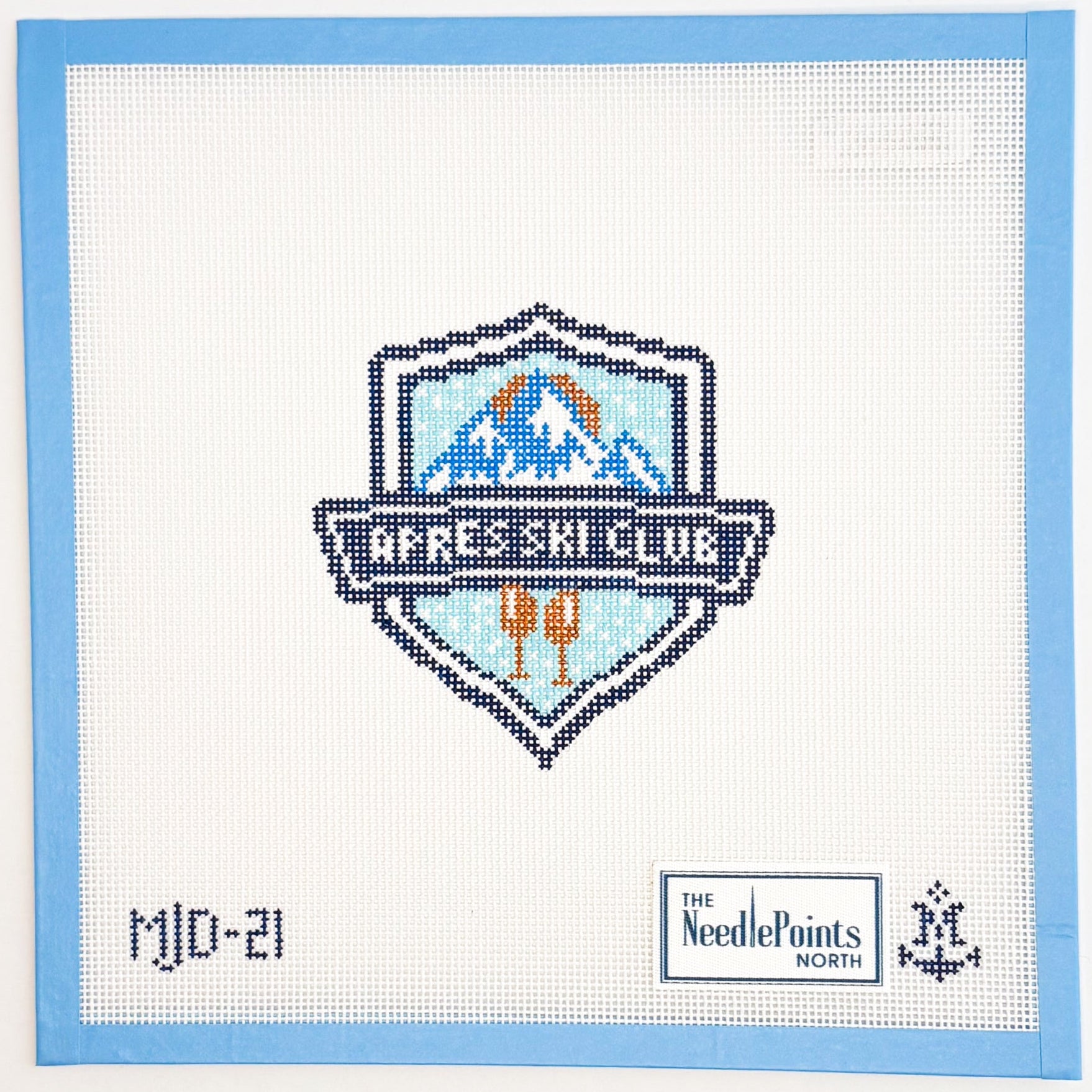 needlepoint design of a mountain landscape with ski poles on a white background, framed by a blue border.