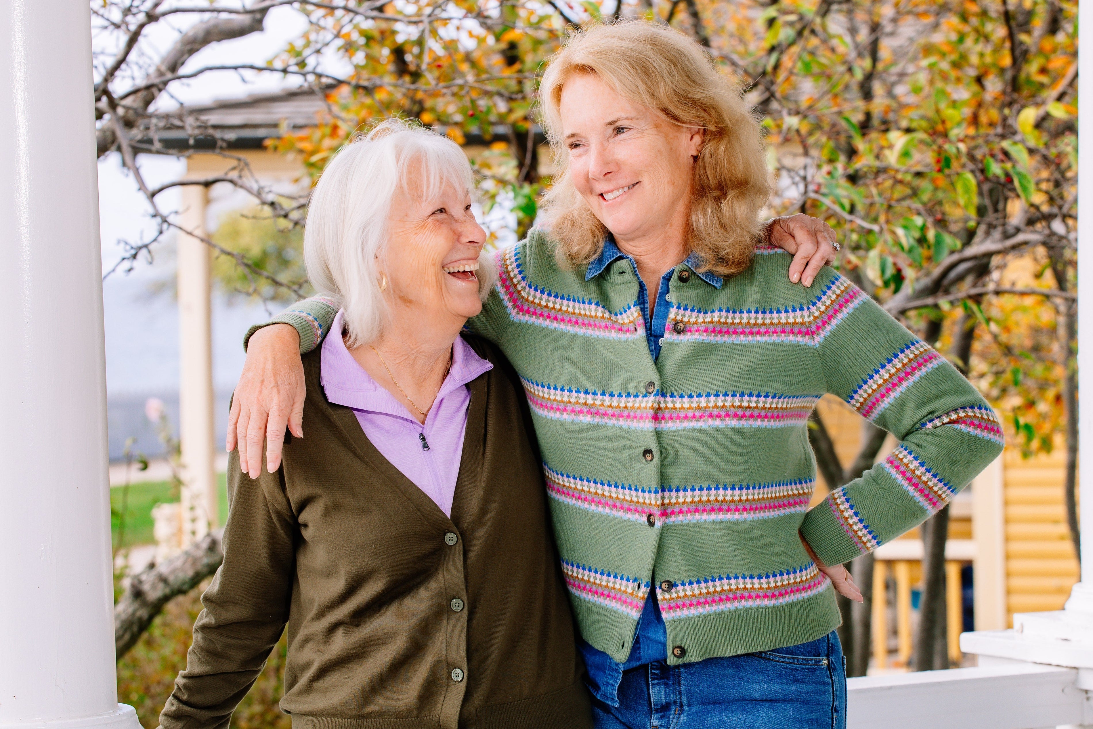 Two women standing on a porch with autumn trees in the background