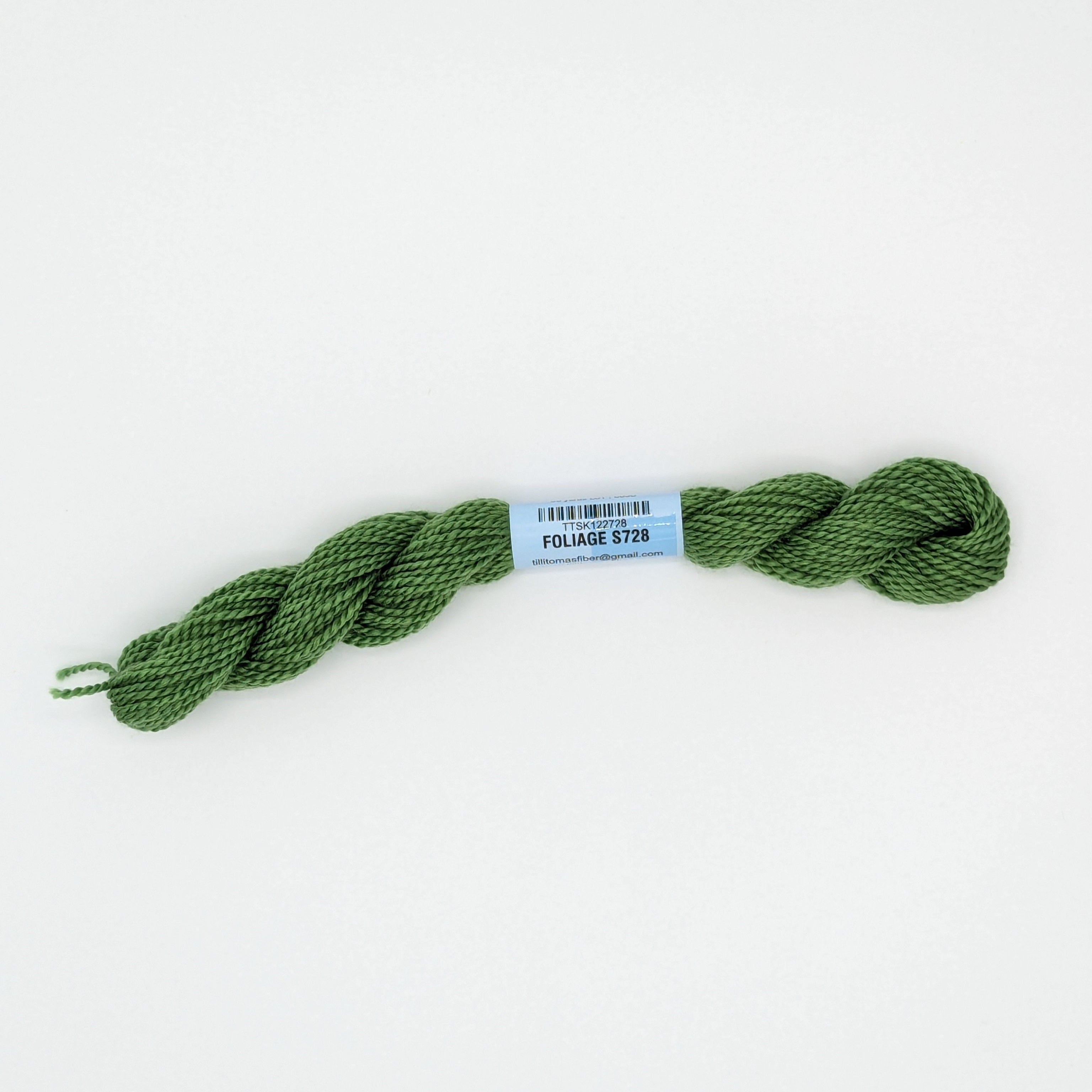 A skein of olive green embroidery floss with a light blue paper label reading 'FOLIAGE' and a barcode, photographed on a clean white background.