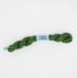 A skein of olive green embroidery floss with a light blue paper label reading 'FOLIAGE' and a barcode, photographed on a clean white background.