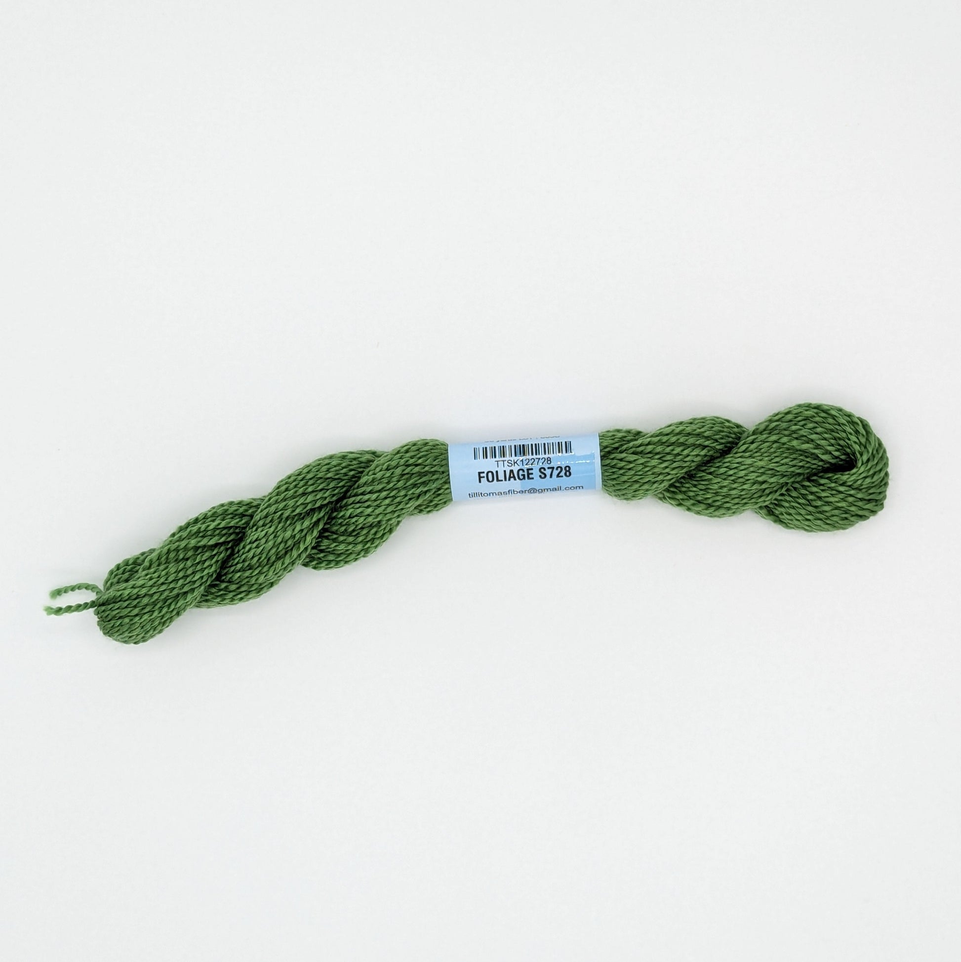 A skein of olive green embroidery floss with a light blue paper label reading 'FOLIAGE' and a barcode, photographed on a clean white background.