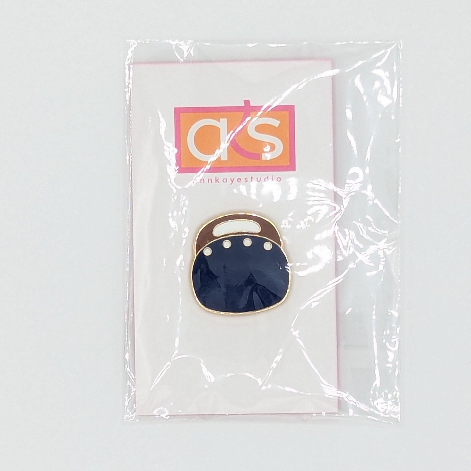 A small enamel pin shaped like a dark navy blue mouth with gold-tone teeth, mounted on a clear display card with a red and gold logo, photographed against a light gray background.