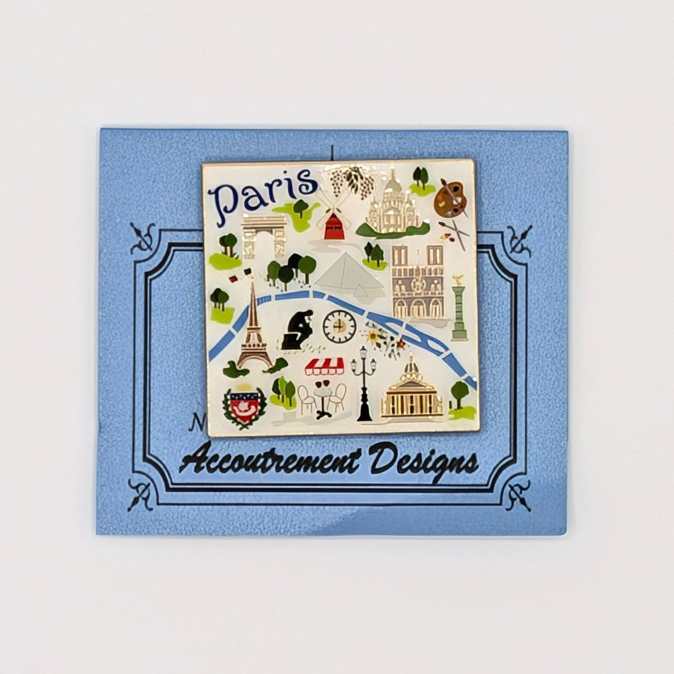 A small square blue card or label featuring a Paris-themed illustrated map design with the text 'Paris' and 'Accompanied Designs' on a plain white background.