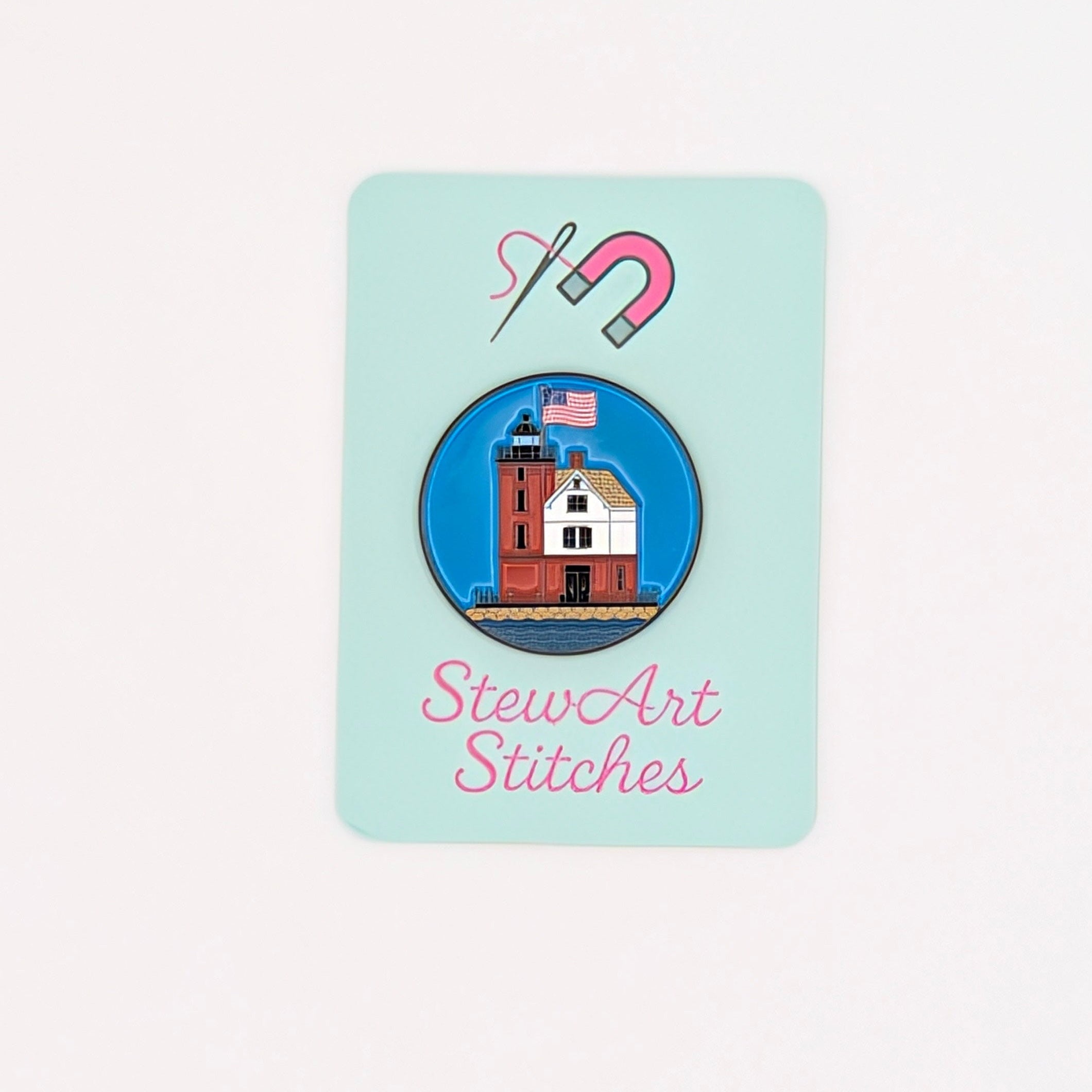 A small mint-green sticker or card from StewArt Stitches featuring a lighthouse illustration and a pink magnet icon, centered on a plain white background.