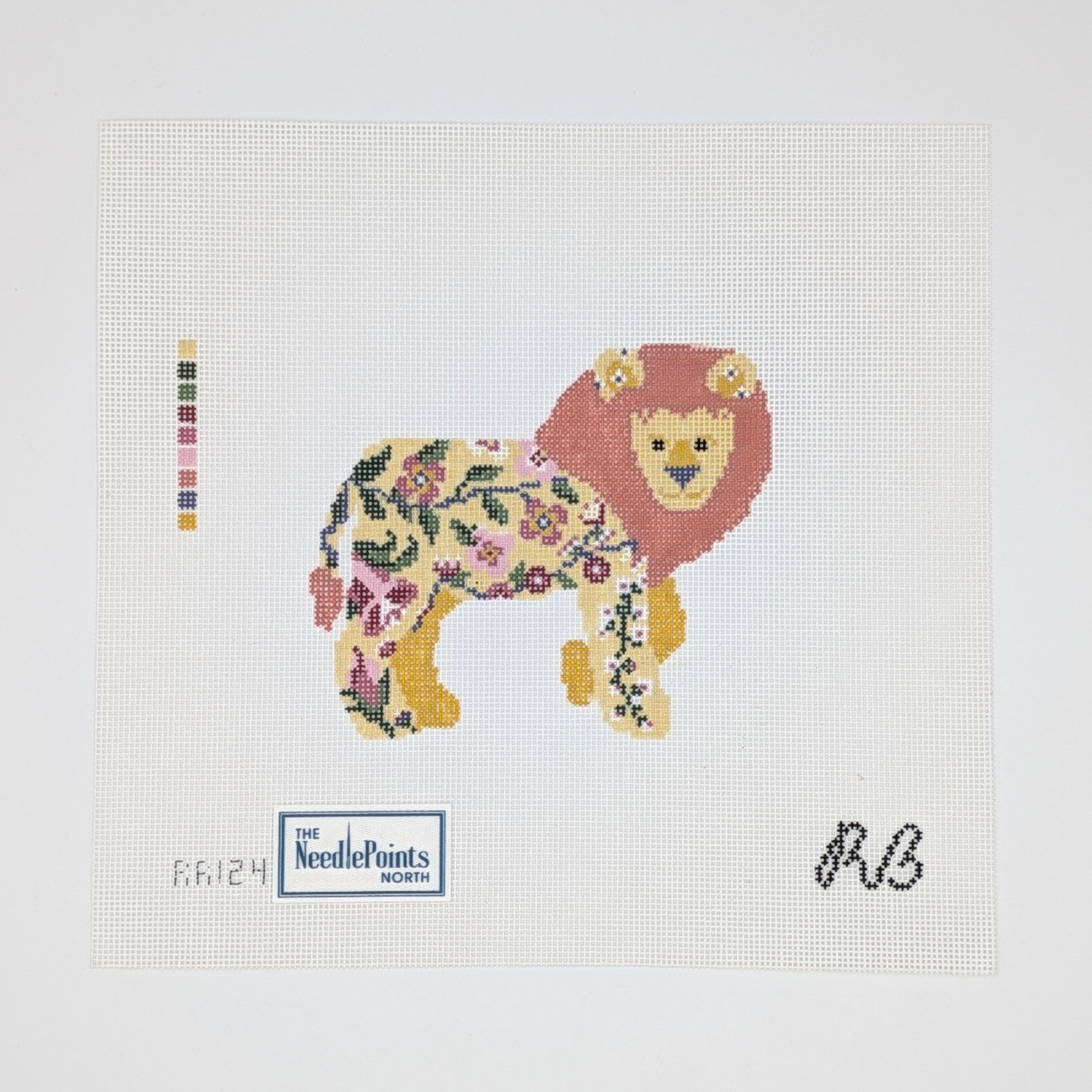 A needlepoint canvas featuring a stylized lion made of floral and botanical patterns, with a red-orange mane, yellow face and paws, and a cream body. The canvas includes a color swatch strip on the left, a 'The NeedlePoints North' logo at the bottom left, and a black monogram 'RB' at the bottom right, all on a white grid background.