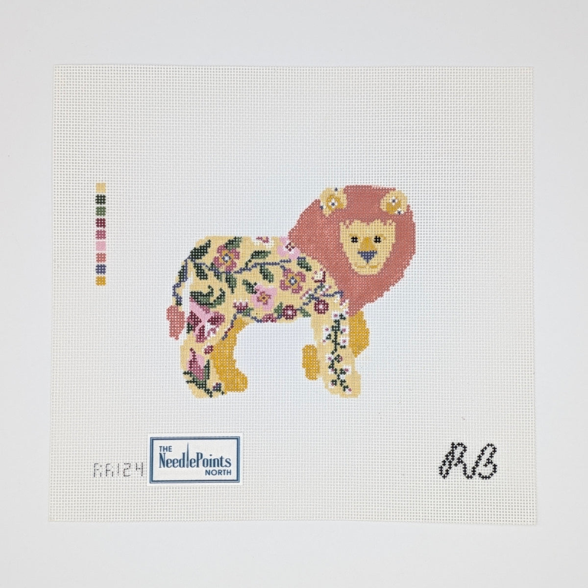 A needlepoint canvas featuring a stylized lion made of floral and botanical patterns, with a red-orange mane, yellow face and paws, and a cream body. The canvas includes a color swatch strip on the left, a 'The NeedlePoints North' logo at the bottom left, and a black monogram 'RB' at the bottom right, all on a white grid background.